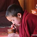 A young monk eating while chanting his morning prayers