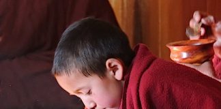 A young monk eating while chanting his morning prayers